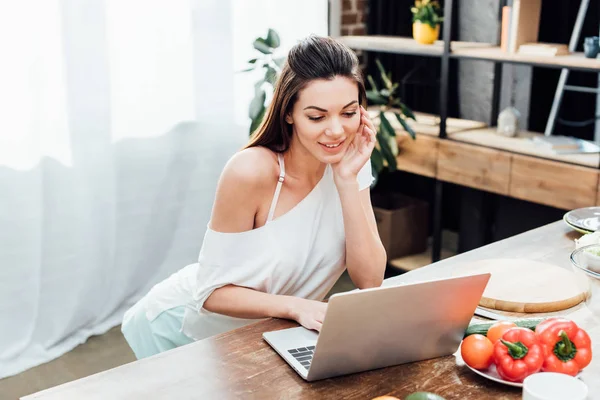 Fille gaie en utilisant un ordinateur portable sur une table en bois dans la cuisine — Photo de stock