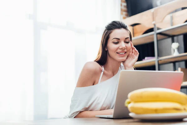 Attraente giovane donna che utilizza il computer portatile a tavola in cucina — Foto stock