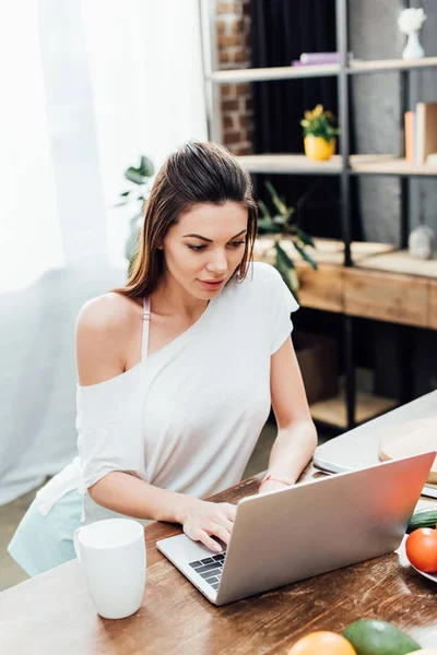 Ragazza allegra utilizzando laptop su tavolo in legno in cucina — Foto stock