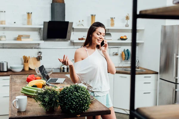 Happy young woman talking on smartphone with smile in kitchen — Stock Photo