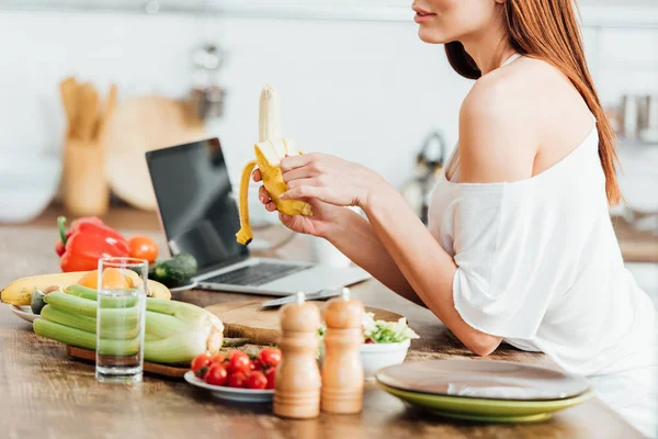 Partial view of young woman holding fresh banana in kitchen — Stock Photo