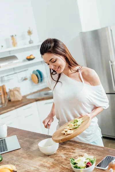 Fröhliches Mädchen hält Schneidebrett mit geschnittenen Bananen und Avocados — Stockfoto