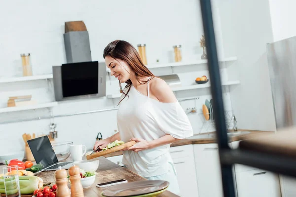 Fille gaie tenant planche à découper avec bananes coupées et avocats — Photo de stock