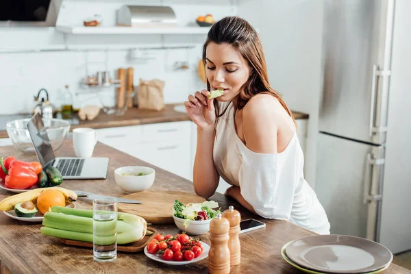 Pensive girl sitting at table and eating salad in kitchen — Stock Photo