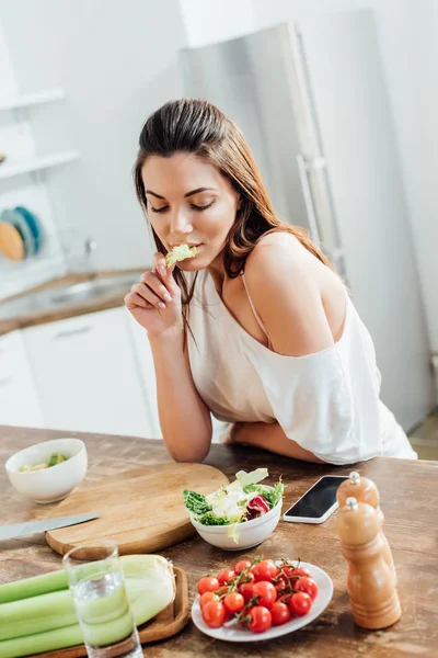 Menina pensativo sentado à mesa e comer salada na cozinha — Fotografia de Stock