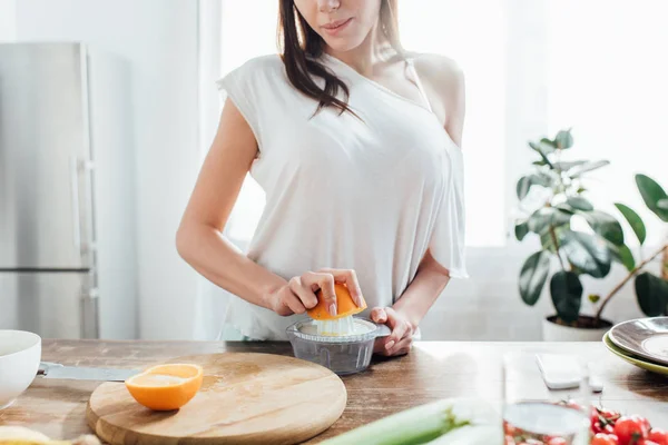 Частичный вид женщины, делающей свежий апельсиновый сок на кухне — стоковое фото