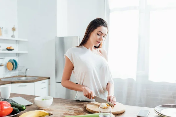 Frau schneidet mit Messer Orange an Tisch in Küche — Stockfoto