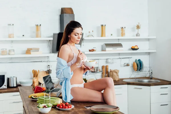 Menina sexy em roupa interior e camisa sentada na mesa e comer salada de frutas — Fotografia de Stock