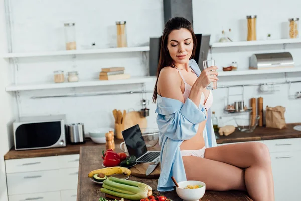 Menina sexy em lingerie branca sentada na mesa e água potável — Fotografia de Stock
