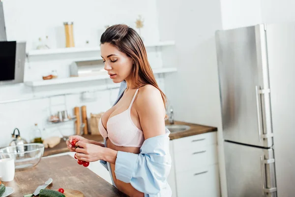 Mulher sensual em lingerie e camisa segurando tomates cereja na cozinha — Fotografia de Stock