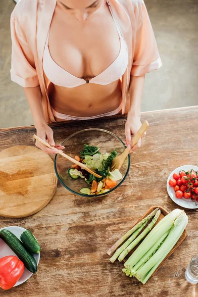 Vista de alto ángulo de la mujer en ropa interior y ensalada de verduras de cocina de casa en la cocina - foto de stock