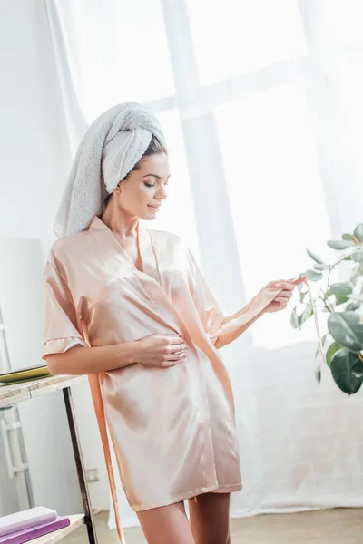 Jeune femme en housecoat avec serviette sur la tête dans la cuisine — Photo de stock