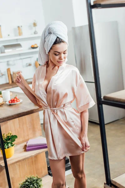 Young woman in housecoat with towel on head looking down in kitchen — Stock Photo