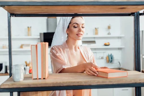 Curious woman in housecoat with towel on head holding book — Stock Photo