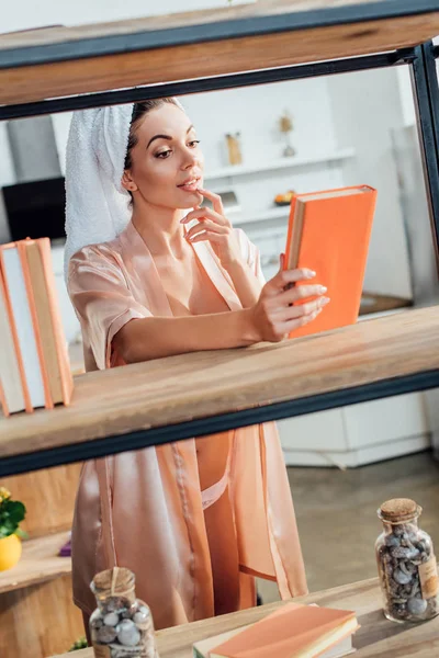 Любопытная женщина в халате с полотенцем на голове, держащая книгу — стоковое фото