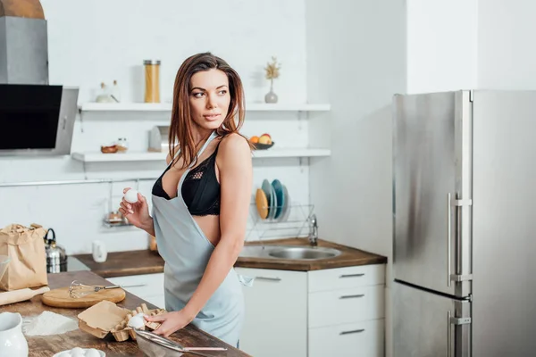 Sexy woman in underwear and blue apron holding eggs in kitchen — Stock Photo