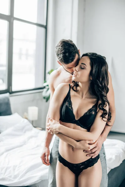 Uomo abbraccio sexy ragazza con gli occhi chiusi in camera da letto — Foto stock