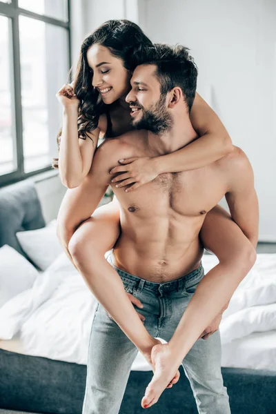 Alegre barbudo hombre piggybacking atractiva mujer con los ojos cerrados — Stock Photo