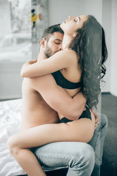 Без сорочки чоловік цілує сексуальну жінку в нижній білизні, сидячи на ліжку — стокове фото