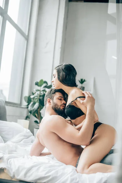 Passionate man kissing and undressing brunette girl on bed — Stock Photo