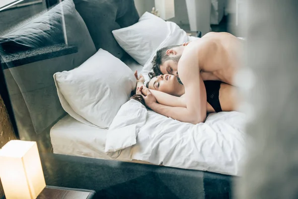 Shirtless man kissing sexy brunette woman on bed — Stock Photo