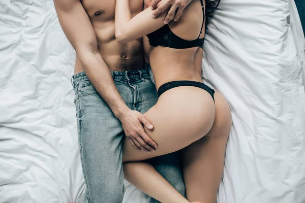 Vue recadrée de l'homme torse nu touchant femme sexy en sous-vêtements noirs tout en étant couché sur le lit — Photo de stock