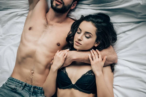 Обрезанный вид мужчины без рубашки, лежащего с привлекательной женщиной в кружевном белье на кровати — стоковое фото