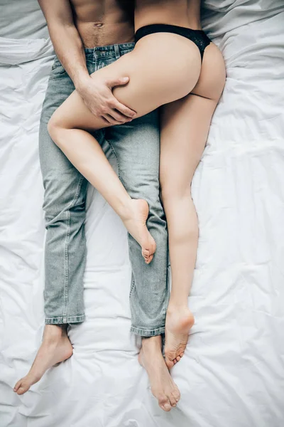 Cropped view of man touching woman in black lingerie while lying on bed — Stock Photo