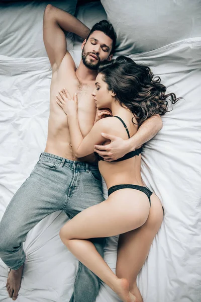 Top view of bearded man lying with attractive woman in black underwear on bed — Stock Photo