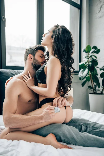 Femme passionnée en sous-vêtements touchant homme tenant préservatif dans les mains — Photo de stock