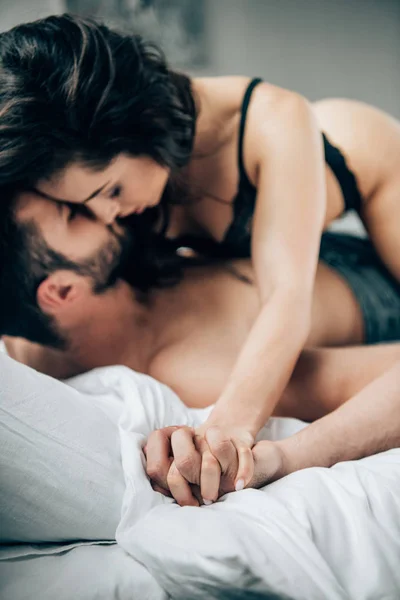 Selective focus of passionate couple holding hands while kissing on bed — Stock Photo