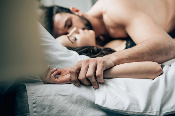 Selective focus of passionate man holding hands with woman while lying on bed — Stock Photo