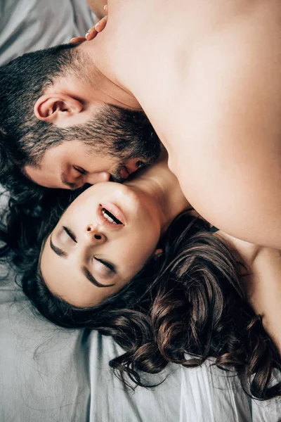 Вид зверху бородатий чоловік цілує привабливу сексуальну жінку на ліжку — стокове фото