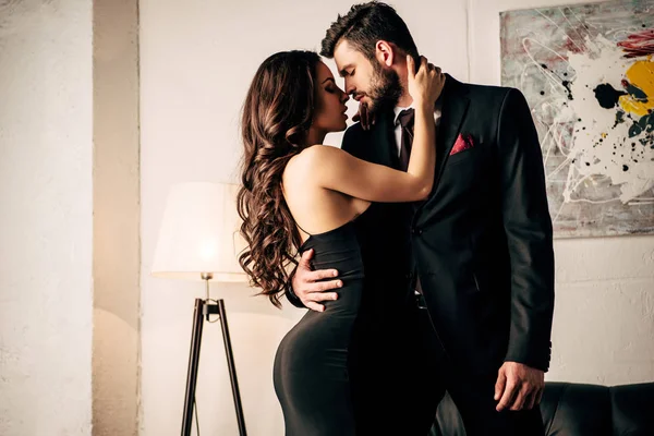 Mulher atraente em vestido preto abraçando com homem apaixonado em terno — Fotografia de Stock