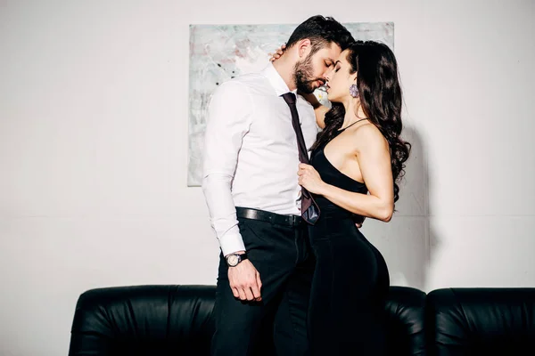 Красива дівчина в чорне плаття цілуватися красеня-чоловіка в костюмі — стокове фото