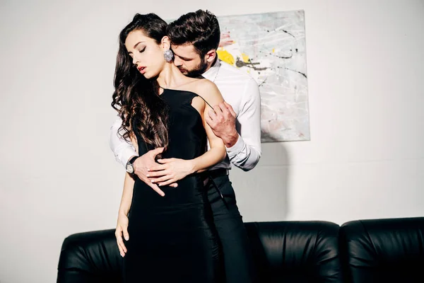 Бородатый мужчина целует и трогает брюнетку женщину в черном платье — стоковое фото