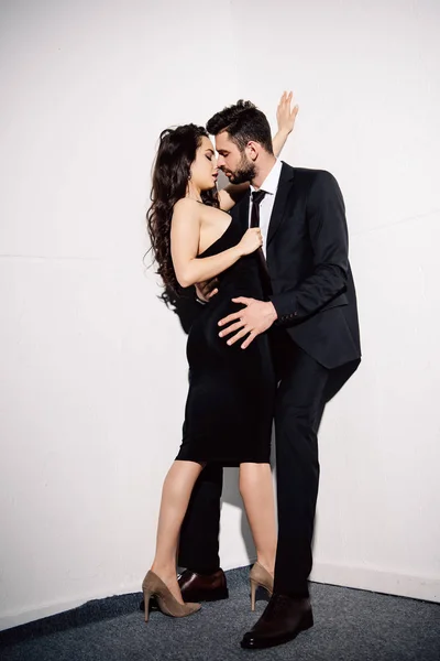 Attrayant brunette femme baisers avec beau homme près de mur blanc — Photo de stock
