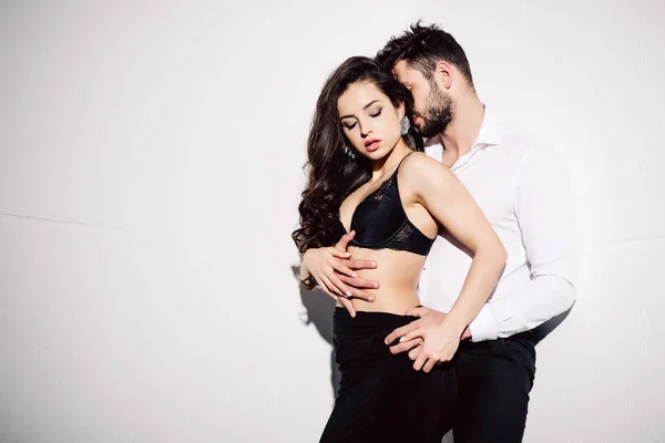 Handsome man touching beautiful woman in black lace bra on white — Stock Photo