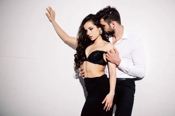 Handsome man undressing beautiful woman in black lace bra on white — Stock Photo