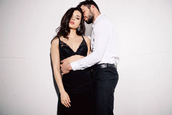 Jolie femme en soutien-gorge noir debout avec bel homme barbu sur blanc — Photo de stock