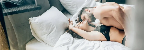 Colpo panoramico di barbuto senza maglietta uomo baciare appassionato bruna donna sul letto — Foto stock