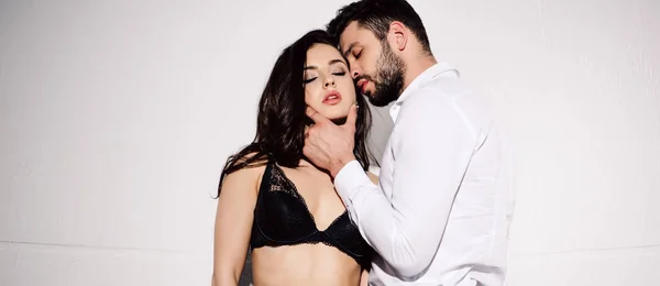 Colpo panoramico di bell'uomo volto toccante di donna sexy in reggiseno nero in piedi su bianco — Foto stock