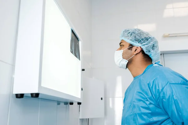 Vista laterale del medico in cappuccio medico e guanto di lattice guardando i raggi X in clinica — Foto stock