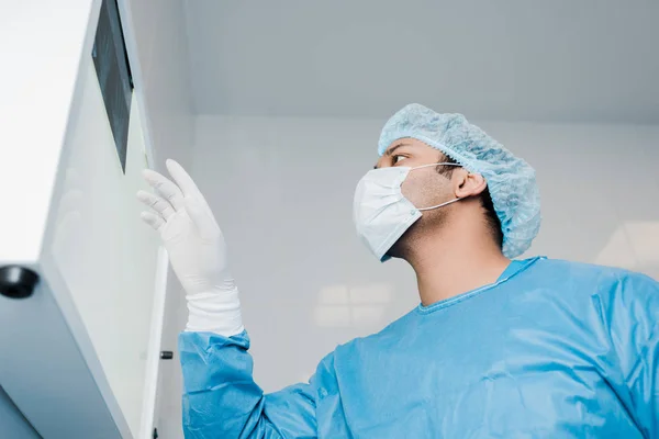 Низкоугол обзора врача в медицинской маске, смотрящего на рентген — стоковое фото