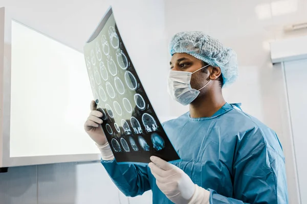 Врач в медицинской маске и латексных перчатках держит и смотрит на рентген — стоковое фото