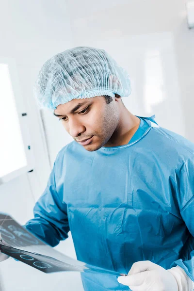 Beau médecin en casquette médicale et uniforme tenant des rayons X dans la clinique — Photo de stock