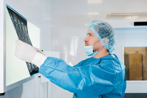 Seitenansicht des Arztes in Mütze und Uniform mit Röntgenaufnahme in der Klinik — Stockfoto