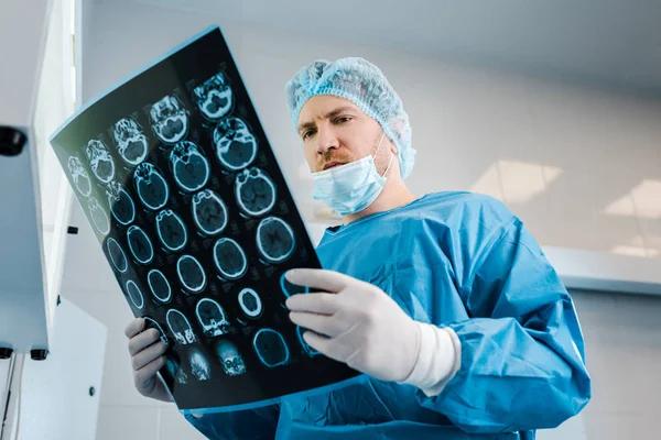 Low angle view of doctor in medical cap and uniform holding x-ray in clinic — Stock Photo