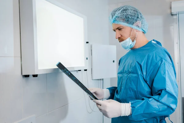 Good-looking doctor in medical cap and uniform holding x-ray in clinic — Stock Photo