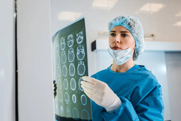 Médecin attrayant en casquette médicale et uniforme tenant des rayons X dans la clinique — Photo de stock